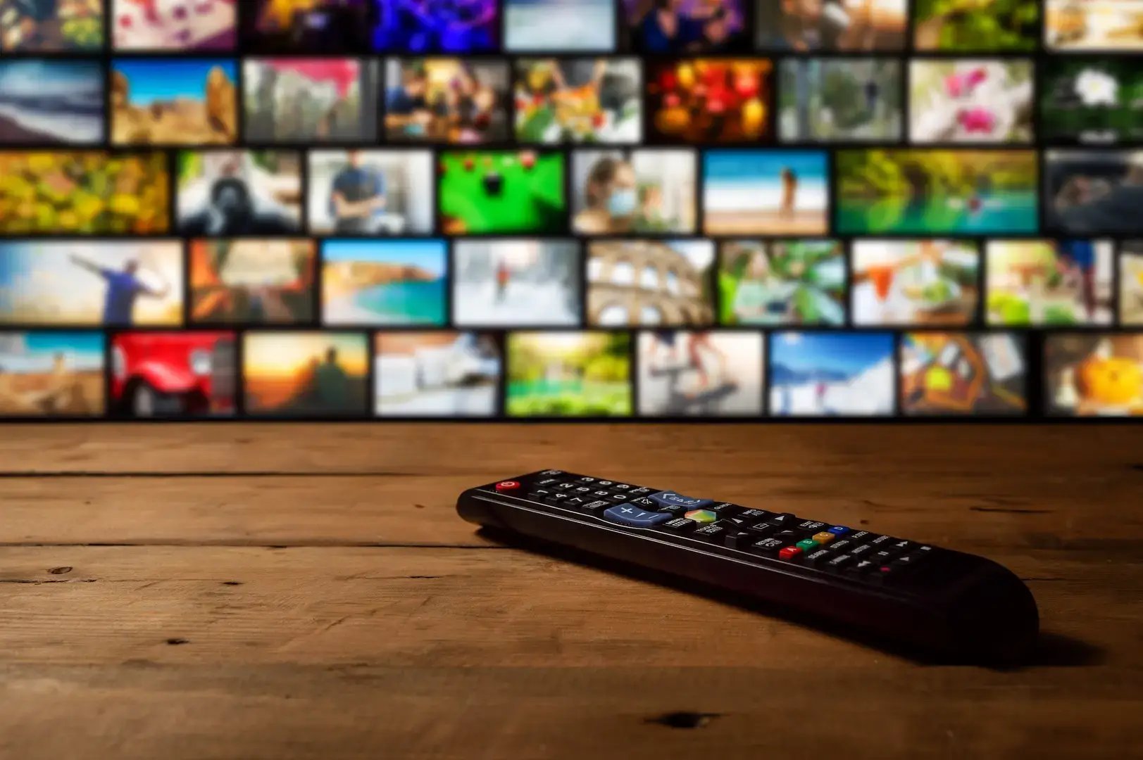 a tv remote is on a wooden table with a background full of TV screens