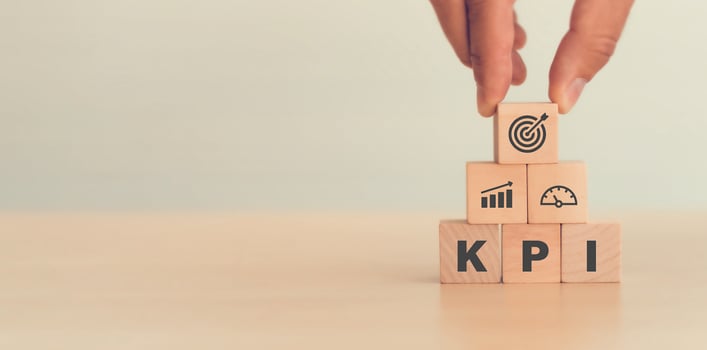 a hand places a pyramid of wooden blocks that spells KPI