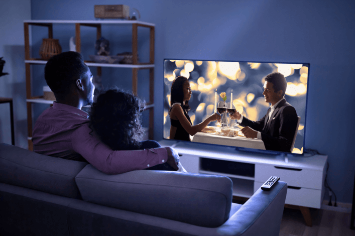 a couple embracing each other on the living room couch watch a romantic show on their TV