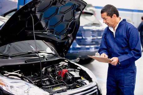 Mechachic checking on a car engine and taking notes
