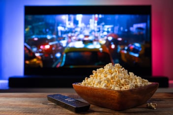 a wooden bowl of popcorn and tv remote are in front of a CTV in the background