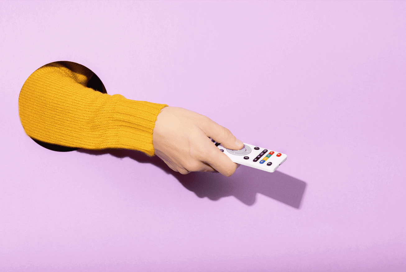 a yellow sleeved arm reaches out from a hole holding a tv remote against a purple background